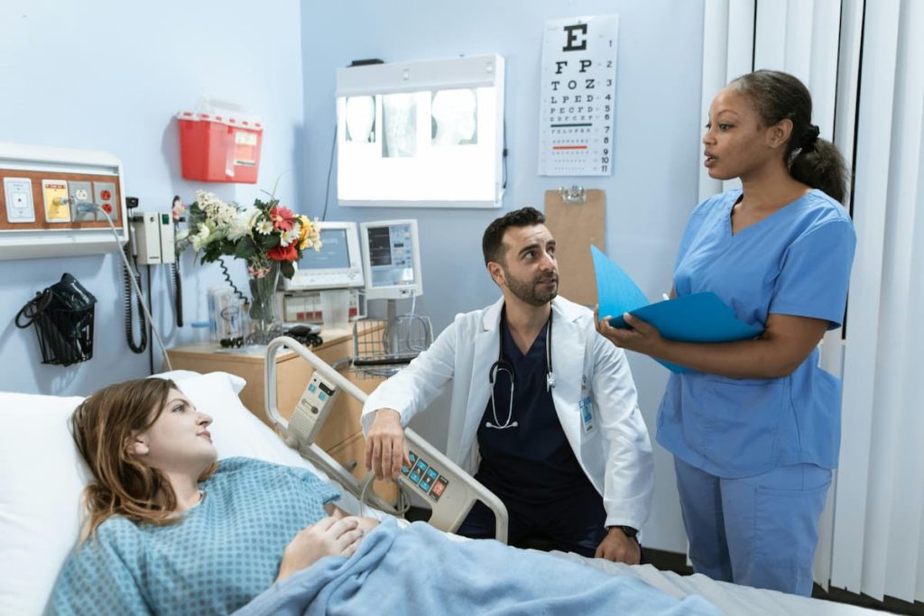 Uma paciente em uma cama de hospital, sendo atendida por dois médicos, que explicam sobre a bolsa de colostomia