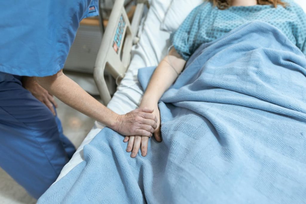 Uma pessoa em uma cama hospitalar com um médico segurando sua mão