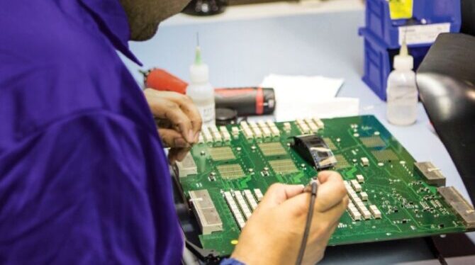 imagem de técnico de óculos e camiseta azul fazendo uma manutenção preventiva em uma placa de equipamento GE Healthcare Manutenção preventiva