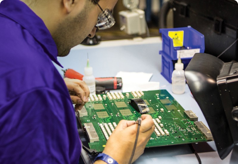imagem de técnico de óculos e camiseta azul fazendo uma manutenção preventiva em uma placa de equipamento GE Healthcare Manutenção preventiva