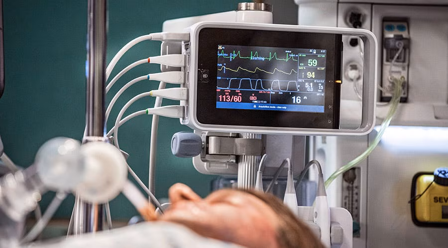 paciente entubado em cama e atrás o monitor ge healthcare